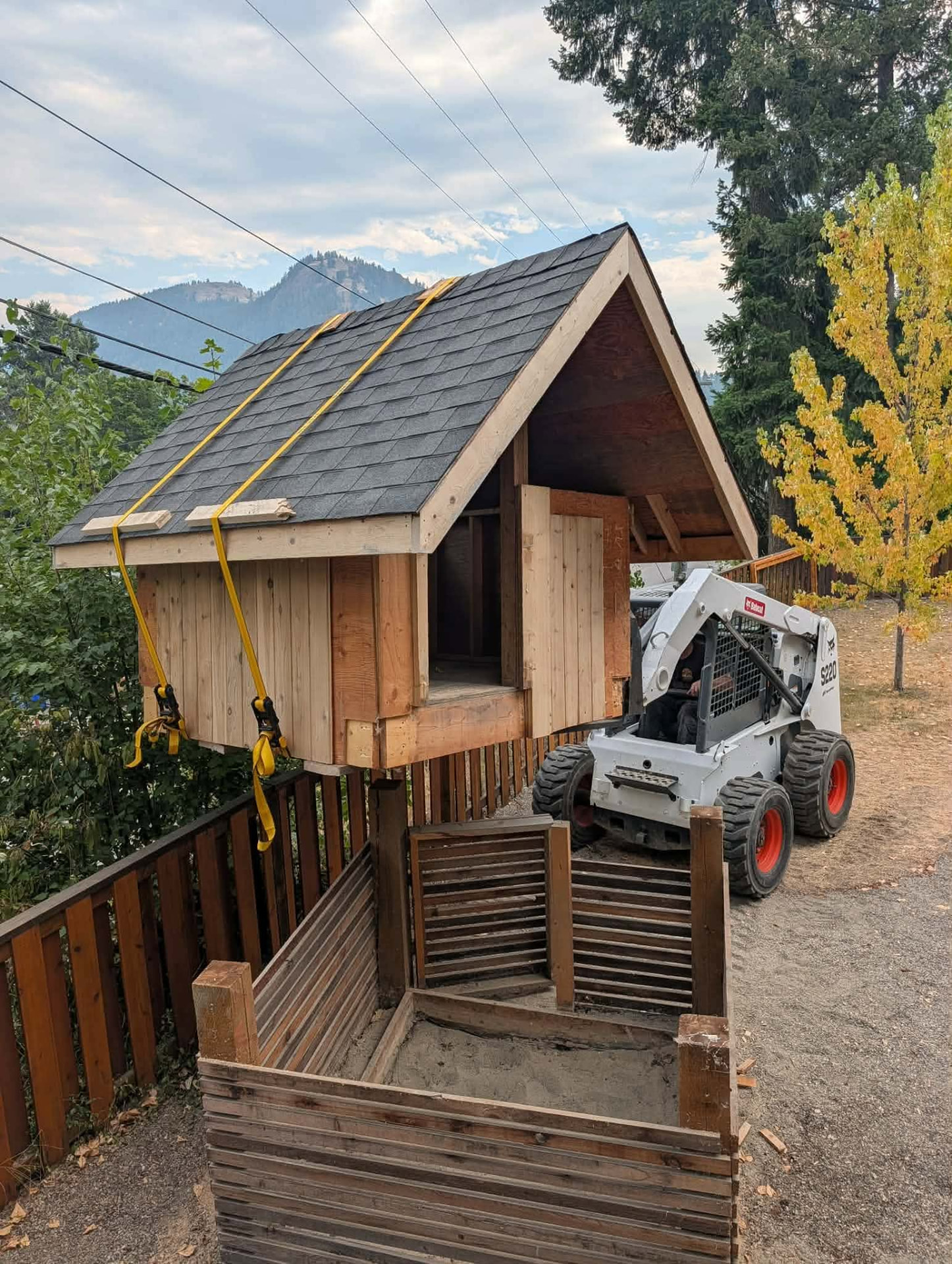 A skid steer being used to load a wooden playhouse.