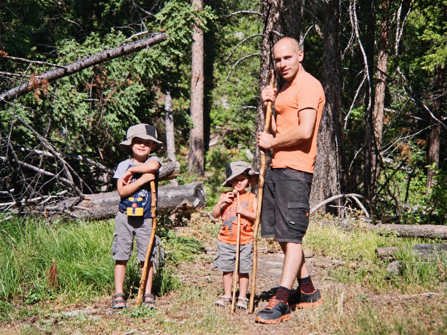 Bradley Weston hiking in the woods with his two sons and their walking sticks.